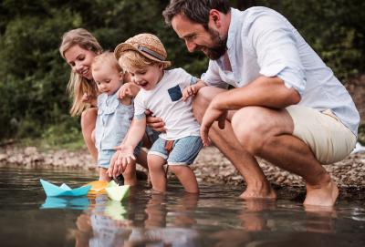 Man and woman with toddlers at a lake sailing paper boats