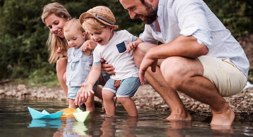 Man and woman with toddlers at a lake sailing paper boats
