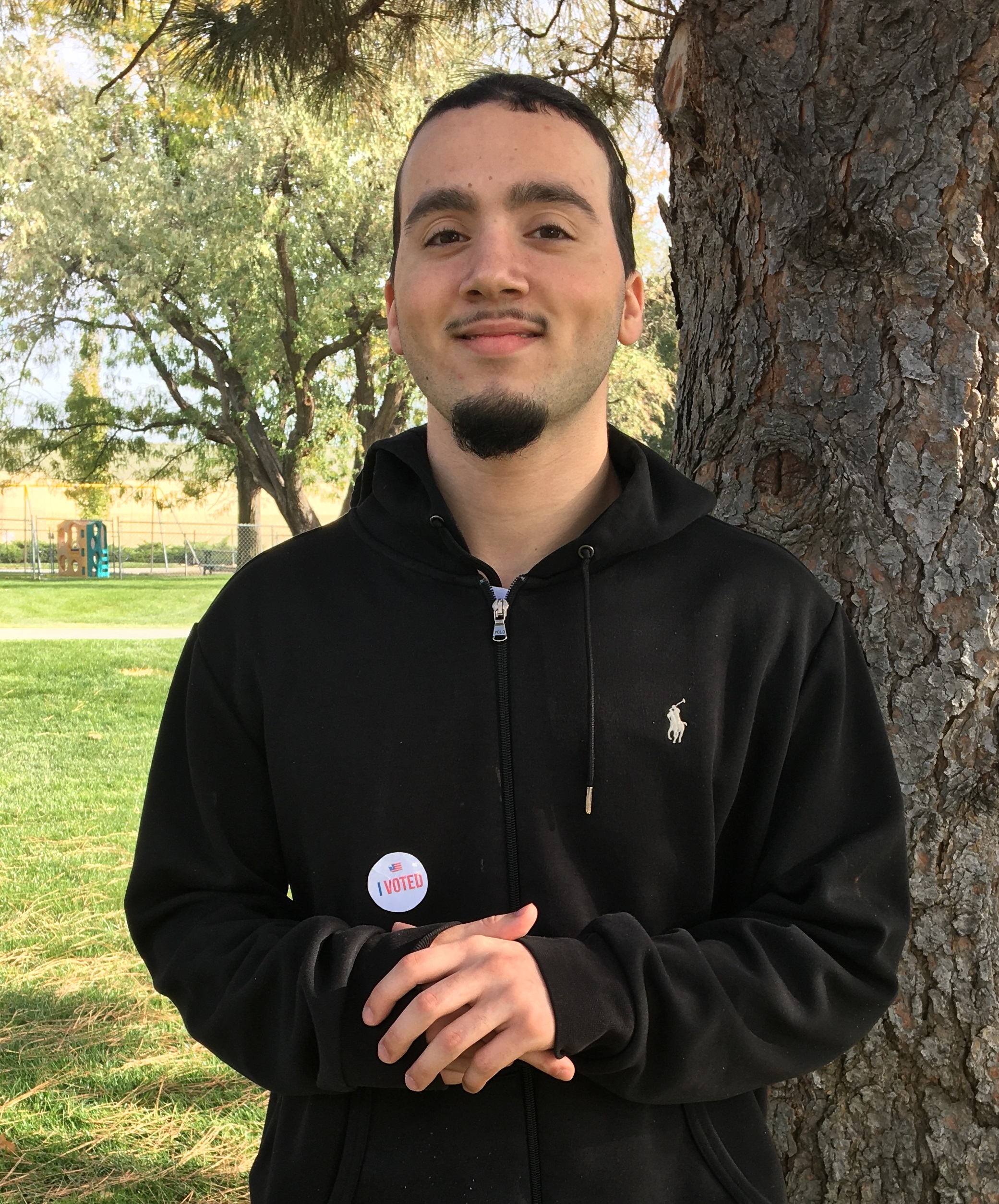 Aaron stands by a tree wearing an "I Voted" sticker. 