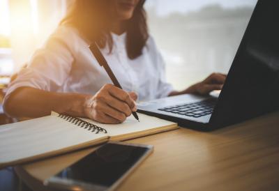 Woman at laptop taking notes on a notepad