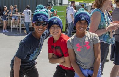 Three kis smiling at the camera with mariner beanies on