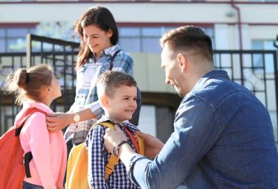 Parents helping young children put on backpacks.