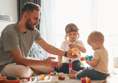 Adult male and toddlers playing with blocks.