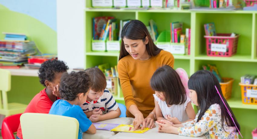 Teacher sitting at table with group of young students