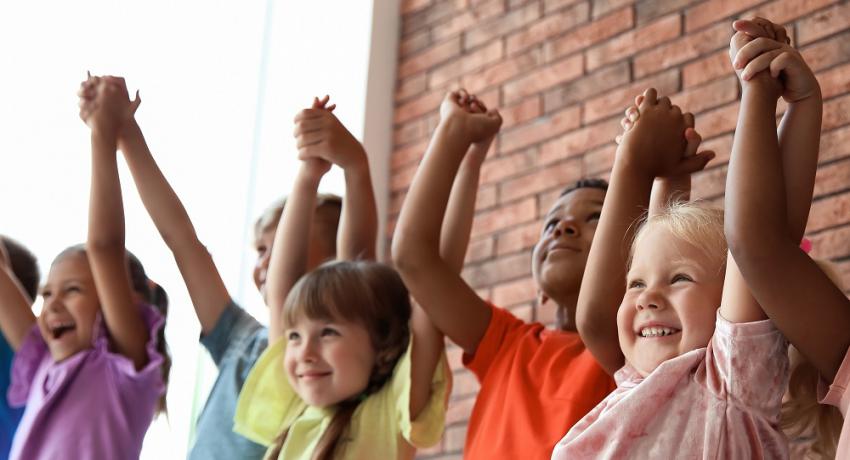 Kids raise their arms and lock hands while smiling. 