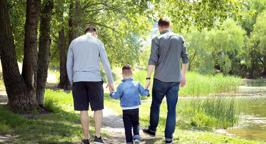 Same-sex parents walking hand in hand with their child in a park. 