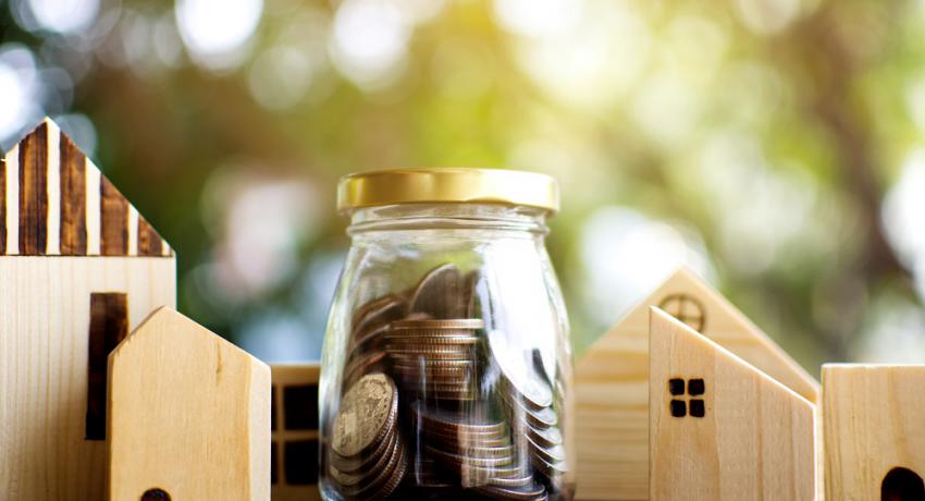 Small houses made of building blocks with a jar of coins in the middle. 