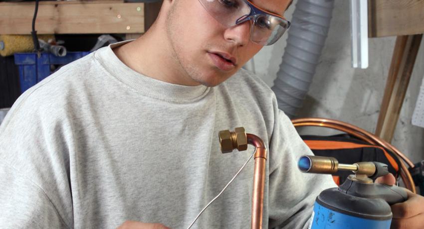 Youth learning to weld copper pipe. 