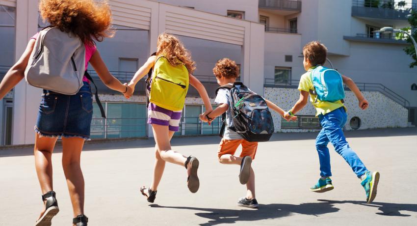 Children wearing backpacks and running in to school