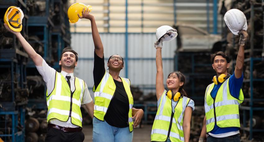 Young people holding their hard hats in a warehouse