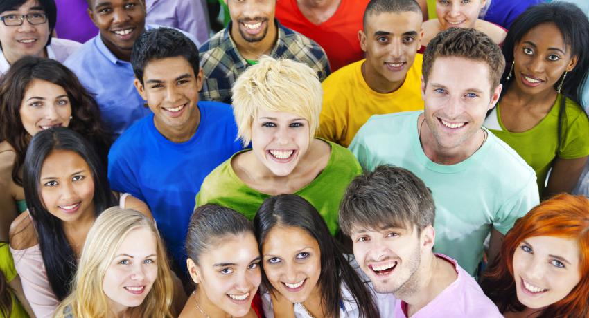 A large group of young adults stand together in colorful shirts smiling. 