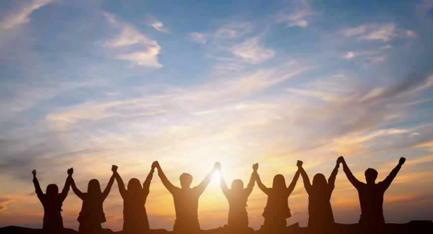 Group of people holding hands up in triumph against the sky. 