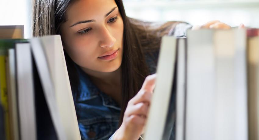 A young woman looks through books at a library.