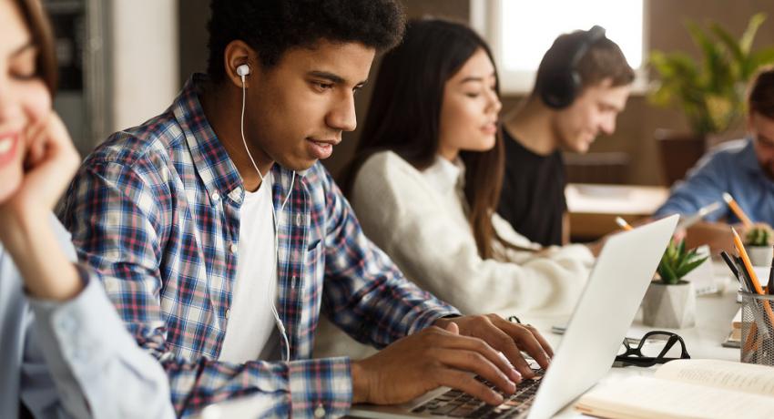 Student learning lessons in school library, using laptop