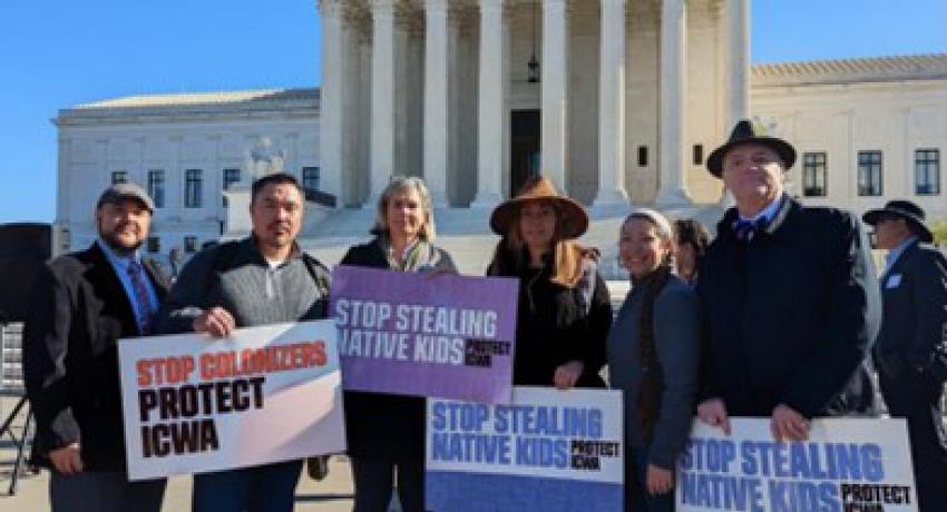 Five people stand outside the steps of the Supreme Court, waving signs in support to uphold the law.