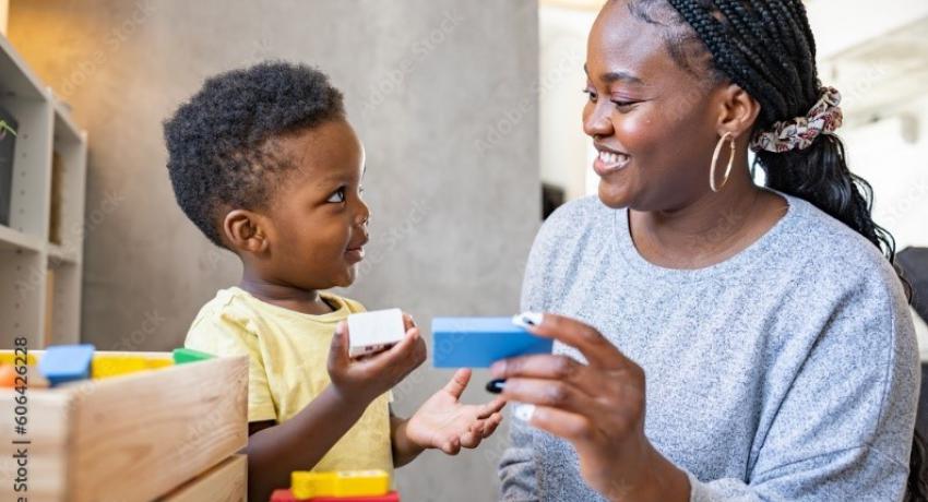 Black mother and child smiling at each other, playing with toys