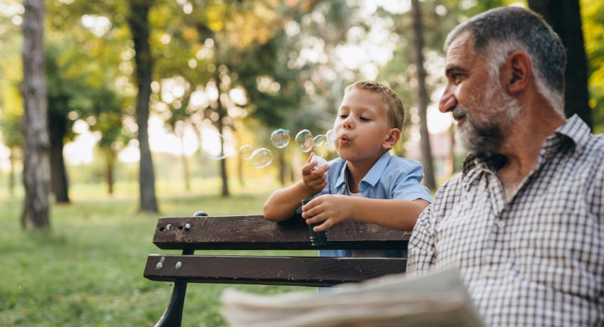 Man reading newspaper on a bench near child blowing bubbles