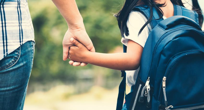 girl with backpack holding her mother hand and going to school 