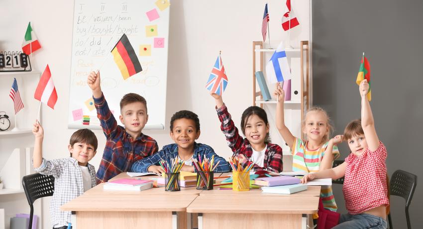 Children in classroom at desk raise flags representing different countries.