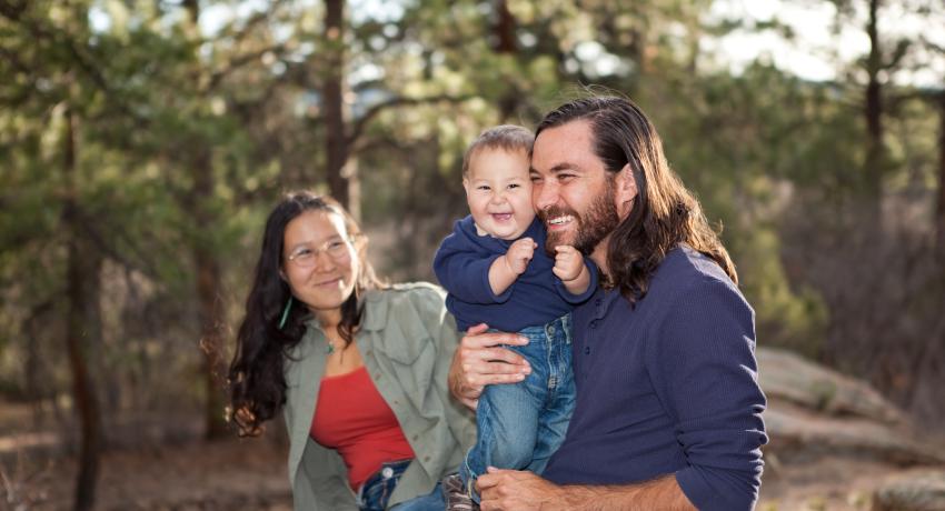 Adult woman and man with smiling child in front of trees