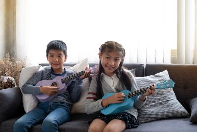 Two children playing ukulele together with smile and happy feeling at studio